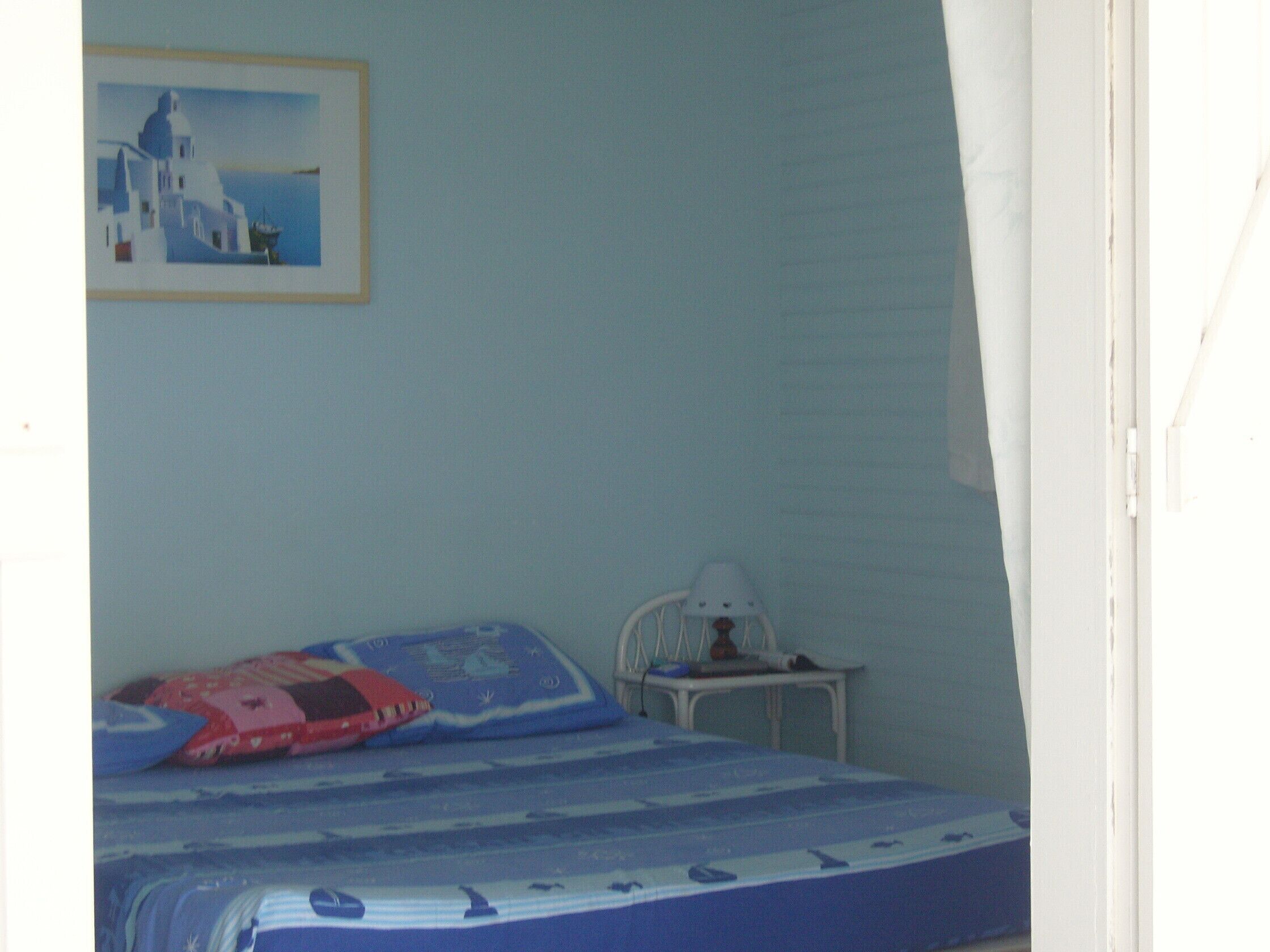 Un dormitorio con una cama, una mesita de noche, una lámpara y un cuadro de una escena costera.