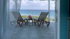 A covered outdoor seating area with two chairs and a table, overlooking a beach.