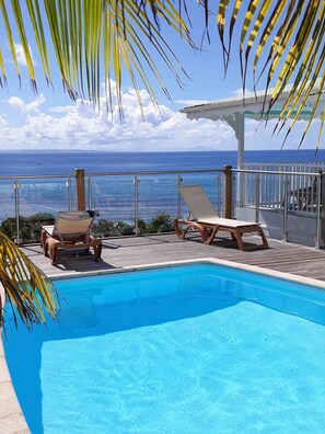 Área da piscina com espreguiçadeiras e vista para o oceano.