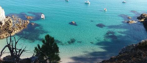 A coastal view with clear turquoise waters, rocky shoreline, and boats.