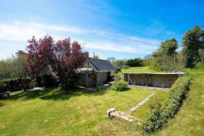 A stone house with a sloped roof, surrounded by a well-maintained lawn and a hedge.