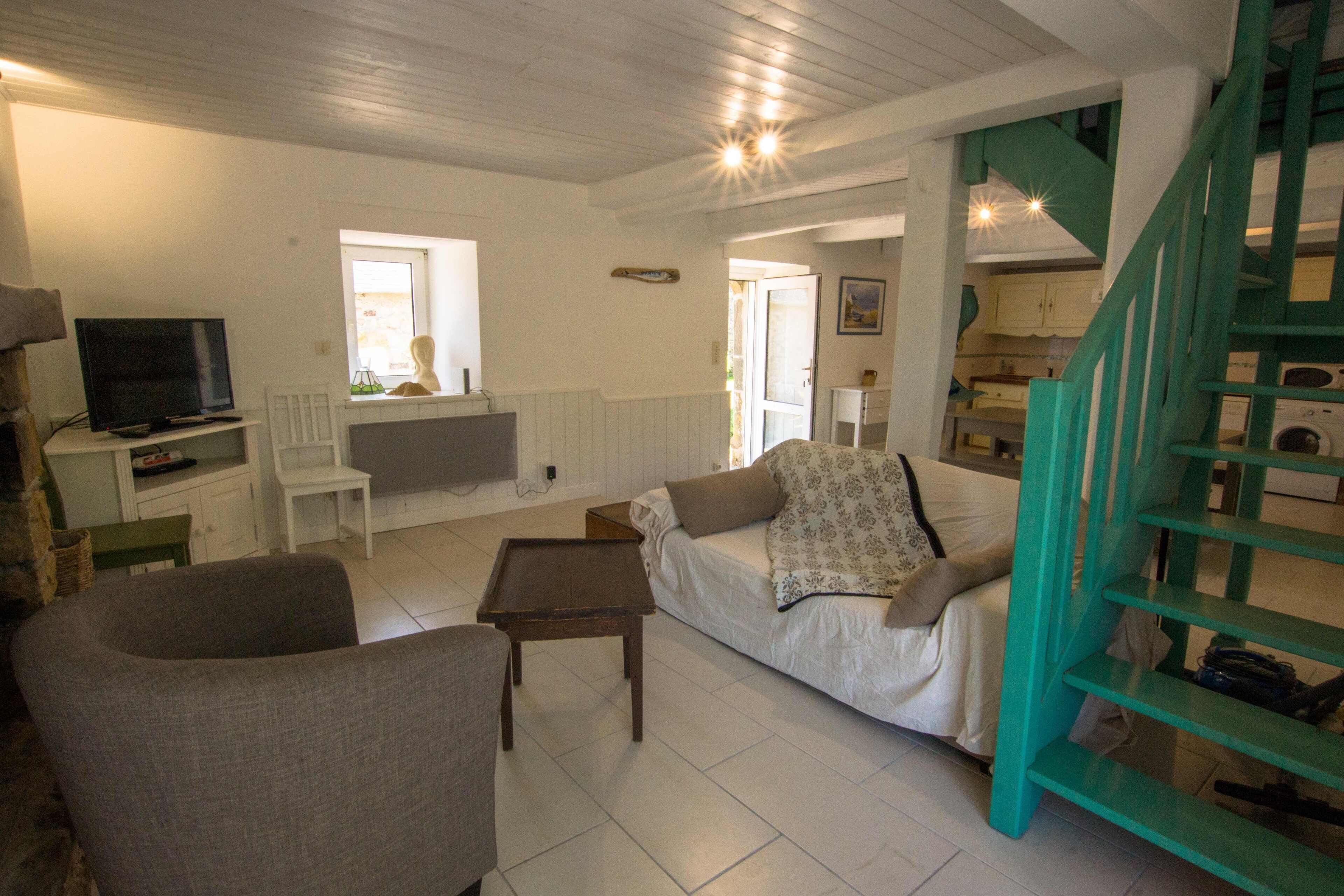 A cozy living room with a sofa, armchairs, a coffee table, a TV, and a staircase with teal railings.