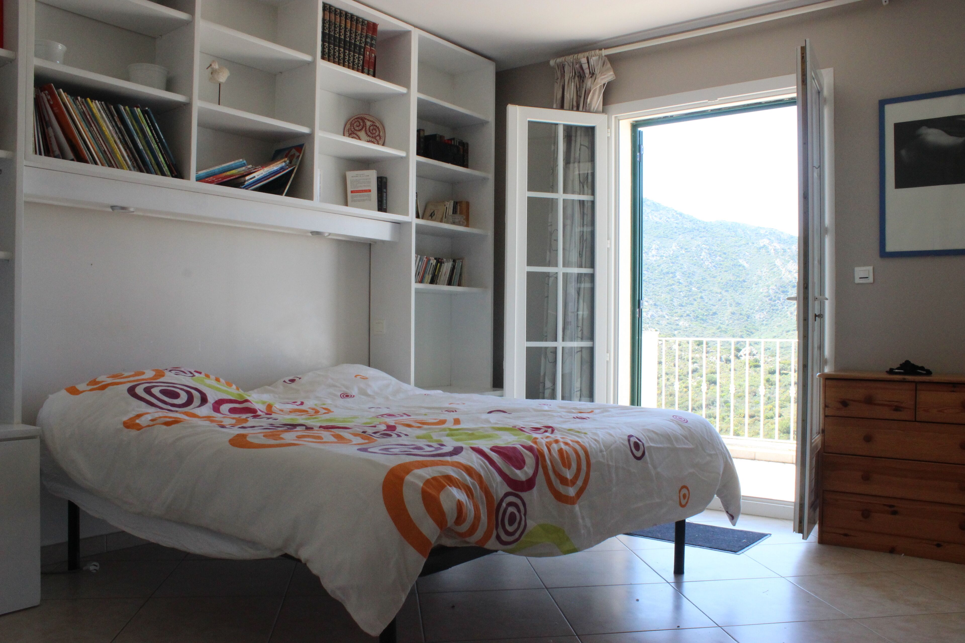 Une chambre à coucher comprenant un lit, une bibliothèque, une commode et un balcon avec vue sur les montagnes.