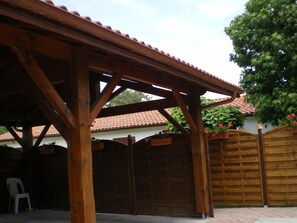 Una pérgola de madera con techo de tejas, un muro de ladrillo y un portón de madera.