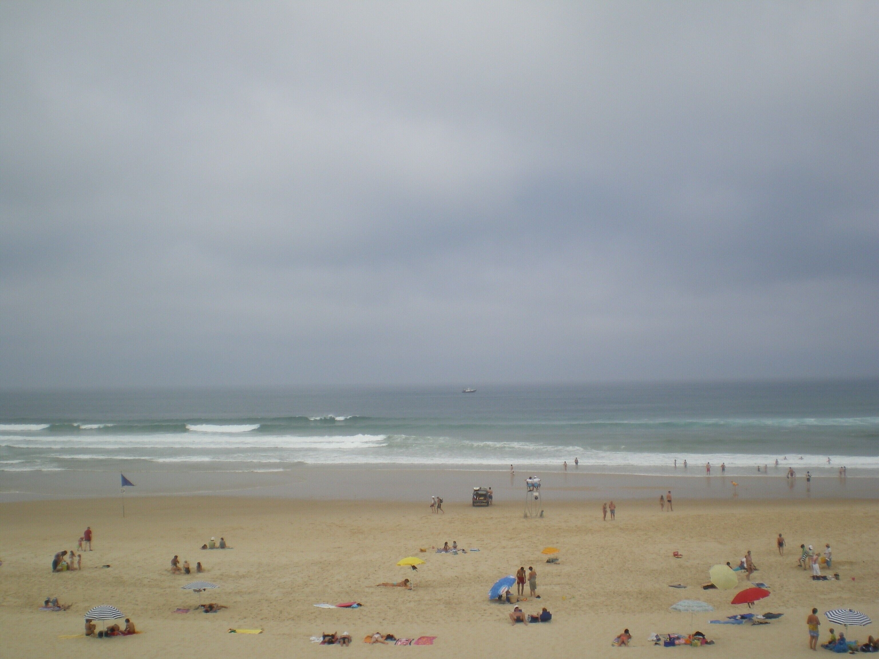 A beach with people sunbathing and swimming, umbrellas, and a lifeguard tower.