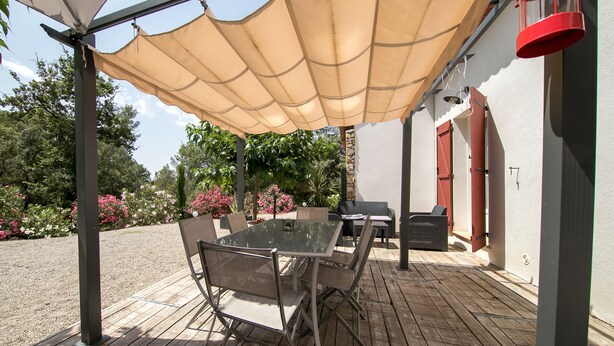 Un patio exterior con una mesa y sillas de vidrio, un toldo color beige y un farolillo rojo.