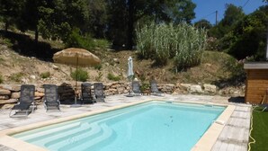 Una piscina rectangular con borde de piedra, rodeada de sillas de descanso y un toldo de paja.