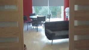 Un umbral abierto que da a un comedor con una mesa y sillas, un sofá y un amplio ventanal con vistas a zonas verdes.