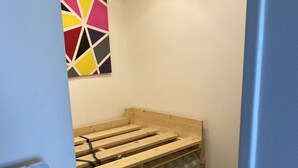Un dormitorio pequeño y ordenado con una cama de madera, un cuadro abstracto y colorido en la pared y un suelo de baldosas.