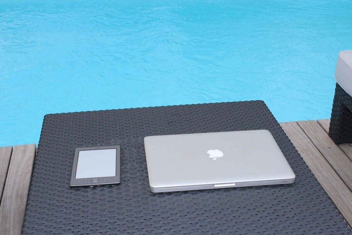 Un laptop e un tablet poggiati su un tappetino strutturato vicino a una piscina.