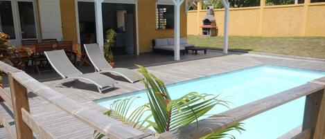 A pool area with a wooden deck, lounge chairs, and a covered seating area.