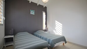 A bedroom with two beds, a nightstand, a lamp, and a window with blinds. - Villa Bel Plaisi - Tropical villa with private pool - 7 pers - Le Moule (Le Moule)