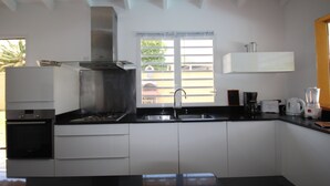 A modern kitchen with white cabinets, a black countertop, a stainless steel range hood, a built-in oven, a double sink, and a window with a view of the outside. - Villa Bel Plaisi - Tropical villa with private pool - 7 pers - Le Moule (Le Moule)