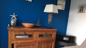 Un mueble de madera con cajones y una repisa frente a una pared azul, una lámpara y un altavoz Sony sobre una mesa.