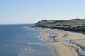 Un paysage côtier avec une plage de sable, un phare et des collines ondulantes.