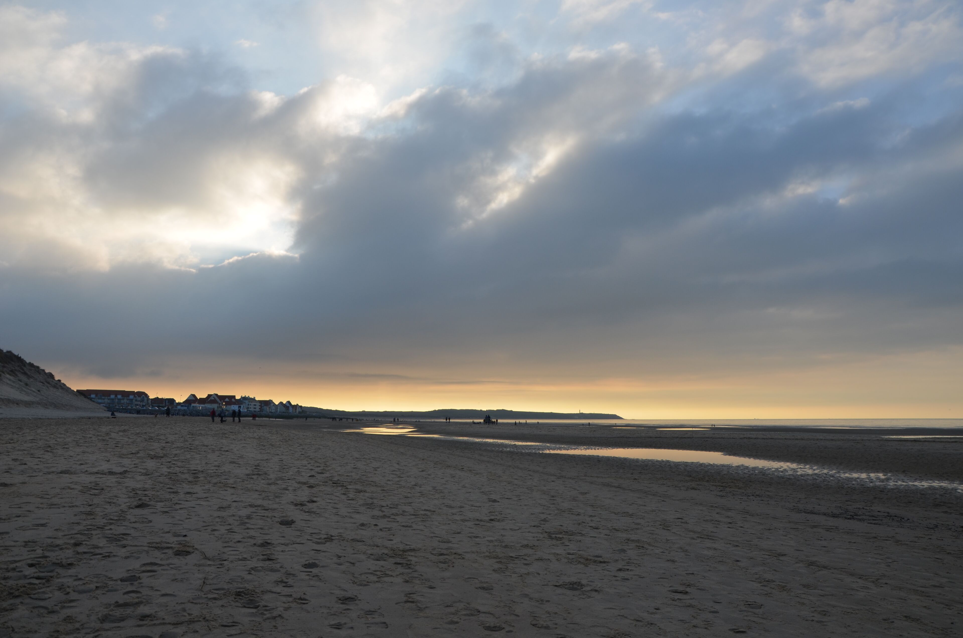 Een strand met een groot zandgebied, enkele mensen en een verre kustlijn met gebouwen.