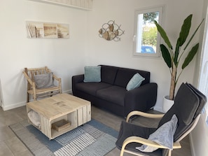 Ein Wohnzimmer mit einem dunkelbraunen Sofa, einem Holztisch, einem grauen Sessel und einer großen Topfpflanze.