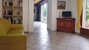 A living room with a yellow armchair, a bookshelf, a TV on a wooden cabinet, and a painting on the wall.