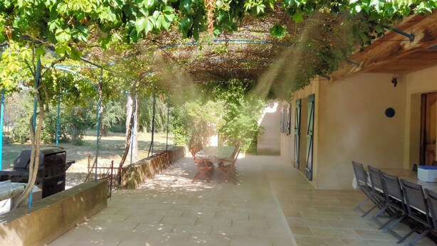 A covered outdoor patio with a pergola, a barbecue grill, and a dining area with chairs and tables.