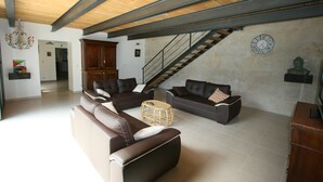 A spacious living room with leather sofas, a wooden ceiling, a staircase, and a clock on the wall.