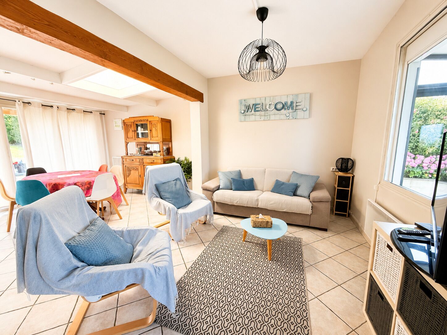 A living room with a sofa, chairs, a coffee table, a cabinet, and a 'WELCOME' sign.