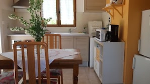 A kitchen with wooden cabinets, a white refrigerator, a microwave, and a sink. There is a wooden dining table with chairs and a vase with flowers. - The cottage Baragnou lantern Nalzen (Nalzen)