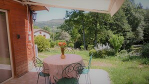 An outdoor patio with a round table and two chairs, a vase with flowers, and a view of a rural landscape with trees and a house in the background. - The cottage Baragnou lantern Nalzen (Nalzen)