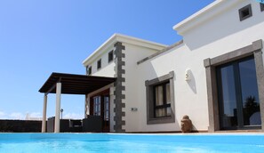 Una villa moderna con piscina, un porche cubierto y un ventanal grande.