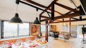 A spacious dining area with a long table set for a meal, wooden beams on the ceiling, and a large window providing a view of the city.