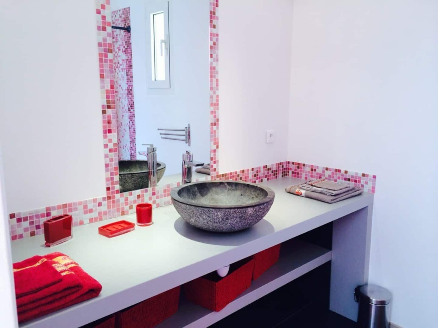 Ein modernes Badezimmer mit einem großen Becken aus Stein, einem Spiegel und einem roten Handtuch auf der Ablagefläche.