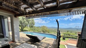 A wooden deck with a pool, lounge chairs, and a hot tub overlooking a scenic landscape.