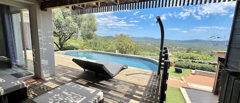 A wooden deck with a pool, lounge chairs, and a hot tub overlooking a scenic landscape.