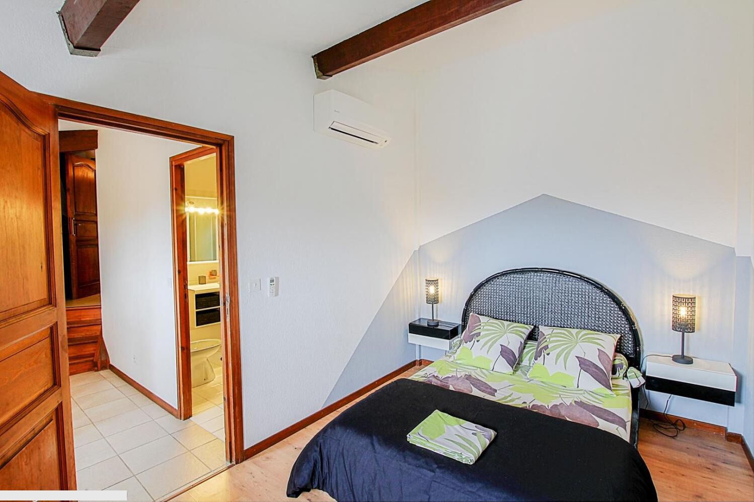 A bedroom with a sloped ceiling, a bed with a headboard, two bedside lamps, and a nightstand.