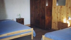 A room with two wooden beds, a wardrobe, a small table with a lamp, and a television on the wall. - Have a breath in our mountains. (La Bresse)