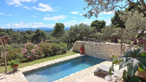 A stone pool with lounge chairs, surrounded by a stone wall and potted plants, overlooking a scenic landscape with trees and mountains. - Charming 2-person gite with pool between Luberon and Alpilles (Cavaillon)