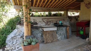 An outdoor kitchen area with a stone wall, a wooden pergola, and a red table with a gas cylinder. - Charming 2-person gite with pool between Luberon and Alpilles (Cavaillon)