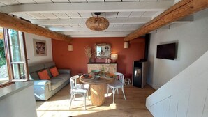 A cozy living room with a wooden ceiling, a round dining table, a sofa, and a TV mounted on the wall. - Charming 2-person gite with pool between Luberon and Alpilles (Cavaillon)