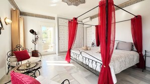 A four-poster bed with red curtains, a white bedspread, and a red pillow. There is a small round table with a lamp and a red cushion. A decorative star is on the ceiling. - Superb villa Sea views Heatable pool 5 min walk to beach & all amenities (La Cala de Mijas)