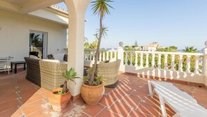 A terrace with wicker furniture, potted plants, and a white balustrade overlooking a coastal area. - Superb villa Sea views Heatable pool 5 min walk to beach & all amenities (La Cala de Mijas)