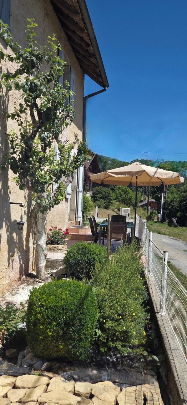 A building with a patio area, outdoor seating, and a tree.
