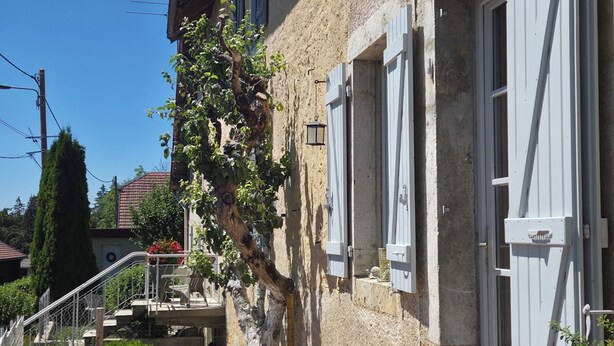 Ein Gebäude mit einer Stein-Fassade, weißen Fensterläden, einer kleinen Außen-Sitzgelegenheit mit Tisch und Stühlen und einer Treppe, die zu einer oberen Ebene führt.