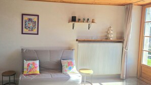 Ein Wohnzimmer mit einer Couch, zwei Kissen, einem gerahmten Kunstwerk, einem kleinen Tisch und einem Regal mit Dekorationsobjekten.
