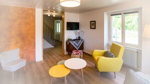 Una sala de estar con un sillón amarillo, un sillón estampado y una mesita redonda. Se ve una escalera al fondo.