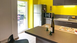 Una cocina moderna con una pared de acento amarilla, una isla central con taburetes de bar, una lámpara colgante y vistas al exterior.