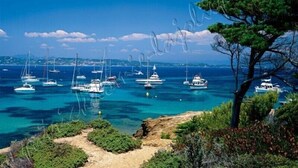 A coastal scene with multiple sailboats anchored in clear blue waters, surrounded by rocky terrain and greenery. - Hyères on the Peninsula Giens, Beach and swimming pool facing Porquerolles *** ! (Hyères)