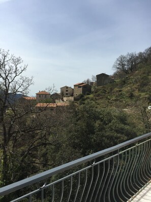 A hillside with several buildings, including a stone house and a larger building with a red roof. - House between sea and mountains (Letia)