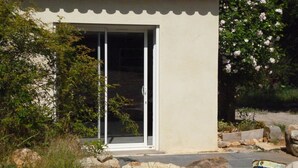 Un edificio con puerta corrediza de vidrio, rodeado de follaje y rocas.