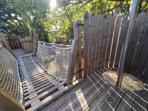 Een houten terras met een touwbrug en een houten omheining.
