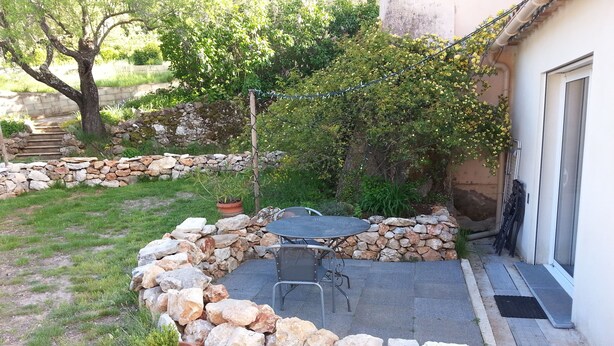 Un patio de piedra con una mesa y sillas, rodeado por un muro de piedra bajo y plantas en macetas.