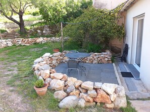 A stone patio with a table and chairs, surrounded by a low stone wall and potted plants.